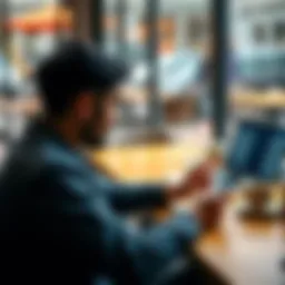 A person reviewing their financial transaction history on a smartphone while sitting at a cafe table, with a laptop and coffee nearby.